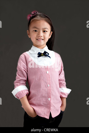 5 Jahre altes chinesisches Mädchen lächelnd, gekleidet in rosa Hemd und Jeans stehend mit Händen in den Taschen Stockfoto