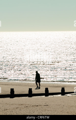 Ein Mann geht am Rand des Meeres an einem Strand in den frühen Morgenstunden Frinton Essex Stockfoto