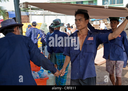 Myanmar, Burma, Yangon. Tally Mann austeilen Tally Sticks, Stauer tragen Sperrholzplatten Boot in Yangon River. Stockfoto