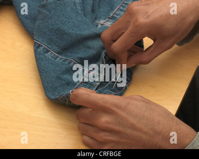 Afro-karibischen Mannhände Saum auf Denimjeans mit Nadel und Faden nähen Stockfoto