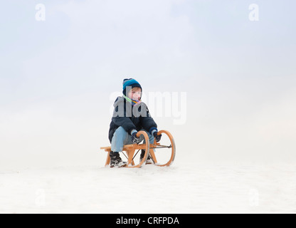 Junge sitzt auf Schlitten im Schnee Stockfoto