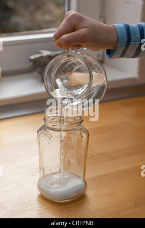 Kinder experimentieren und Kristalle wachsen. Schritt 2: Wasser in Glas mit Salz Stockfoto