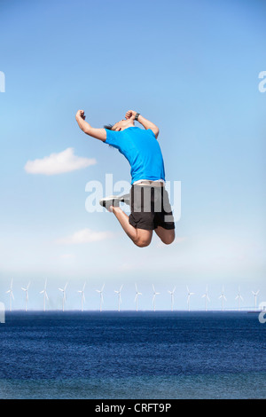 Mann springt vor Freude über Windkraftanlagen Stockfoto