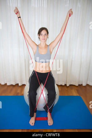 junge Frau, die Übungen mit Theraband auf Gymnastikball sitzend Stockfoto