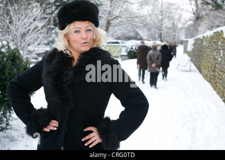 blonde Frau trägt schwarzen Pelzmantel und Pelzmütze stehen im Schnee Stockfoto