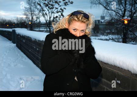 blonde Frau im schwarzen Mantel an einem kalten Wintertag Einfrieren Stockfoto
