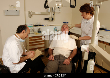 Zahnmedizinische Fachangestellte bereitet eine ein älteren männlichen Patienten für die Behandlung als Zahnarzt untersucht den Patienten Zahnbogen. Stockfoto