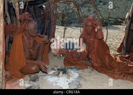 traditionelle Dorf Purros, Himba Frauen rauchen vor einer Hütte, Namibia, Purros Stockfoto