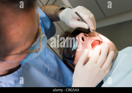 Tragen von Schutzbrillen und Mundmaske Zahnarzt untersucht die Zähne des jungen männlichen Patienten, auch mit besonderen Schutzbrille. Stockfoto