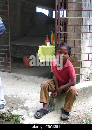 Kleiner Junge sitzt vor Garage er in dem lokal verkauft produzierte Alkohol nach niedergeschossen, Haiti, Provinz de l ' Ouest, Kenskoff, Port-Au-Prince Stockfoto