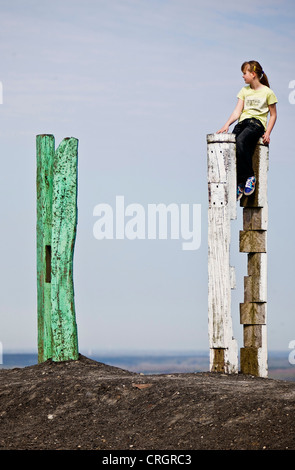 Mädchen sitzen auf einem Totem auf Halde Haniel, Deutschland, Nordrhein-Westfalen, Bottrop Stockfoto