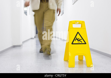 Mann vorbei Warnschild in einem Korridor sagen "Achtung - Rutschgefahr" Stockfoto