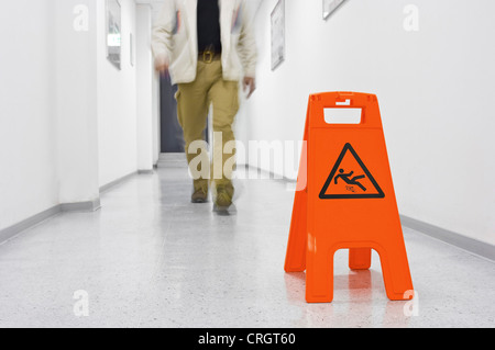 Mann vorbei Warnschild in einem Korridor sagen "Achtung - Rutschgefahr" Stockfoto