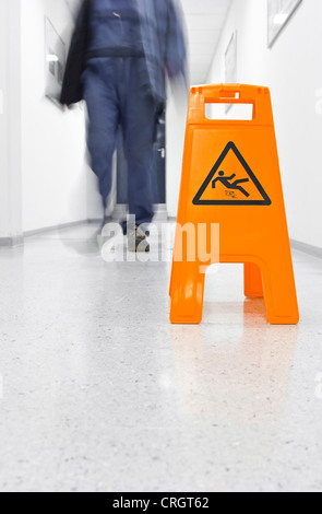 Mann vorbei Warnschild in einem Korridor sagen "Achtung - Rutschgefahr" Stockfoto