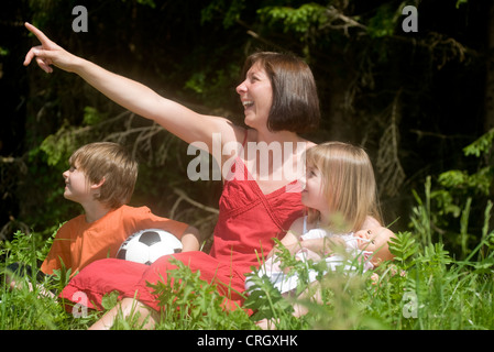 Mutter mit Sohn und Tochter sitzen in der Wiese Stockfoto