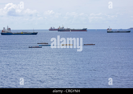 Teams an der jährlichen Falmouth Gig Club Regatta Rennsport einander neben Handelsschifffahrt in Falmouth Harbour UK im Jahr 2011 Stockfoto