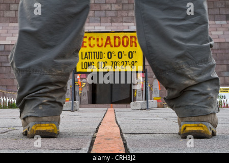 Ein Mann stand über dem Äquator, einen Fuß in der nördlichen und südlichen Hemisphäre in der Nähe von Quito, Ecuador. Stockfoto