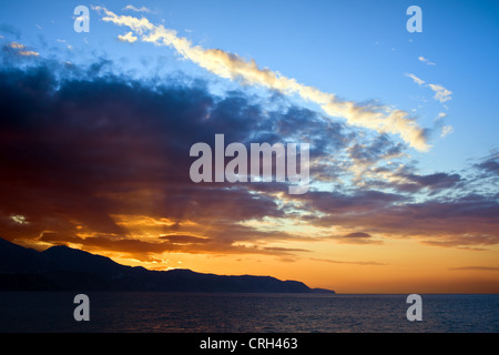 Letzten Sonnenstrahlen durchscheinen Wolken über dem Meer bei Sonnenuntergang an Costa Del Sol in Spanien. Stockfoto