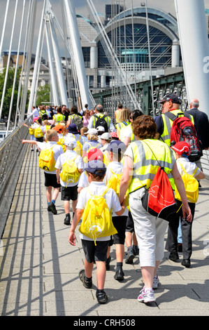 Kinder auf Klassenfahrt begleitet über Fußgängerbrücke alle Warnschutz Jacke tragen Stockfoto