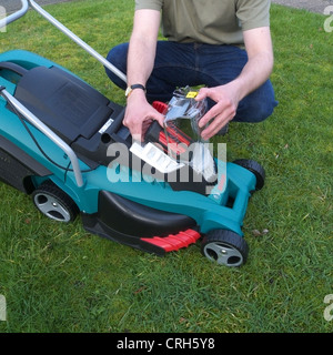 Kaukasischen Mann ändern einen Akku auf eine Bosch wiederaufladbare elektrische Rasenmäher Modell veröffentlicht Stockfoto