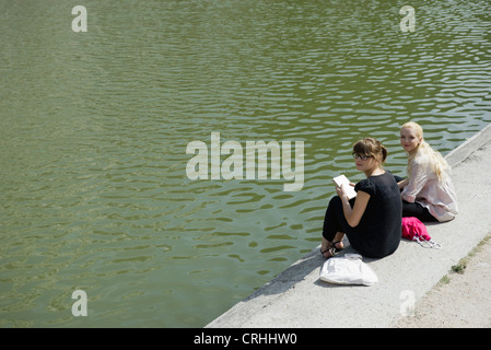 Junge Frauen zusammensitzen am See Stockfoto