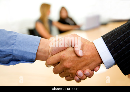 Business Handshake in einem Büro mit Team hinter Stockfoto