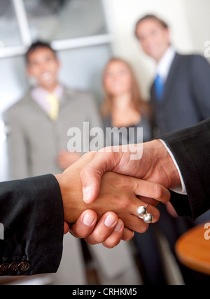 Business Handshake in einem Büro mit Team hinter Stockfoto