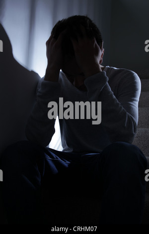 Junger Mann sitzt auf der Treppe, seine Hände auf seinen Kopf in Verzweiflung. Stockfoto