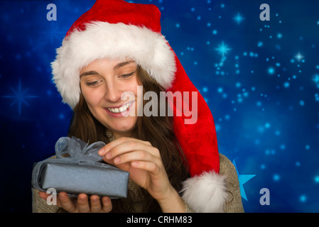 Junge Frau trägt Weihnachtsmütze, Weihnachtsgeschenk öffnen