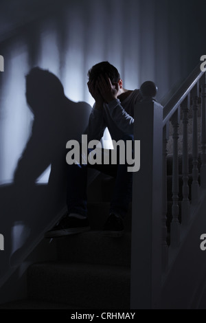 Junger Mann sitzt auf der Treppe, seine Hand bedeckte sein Gesicht. Stockfoto