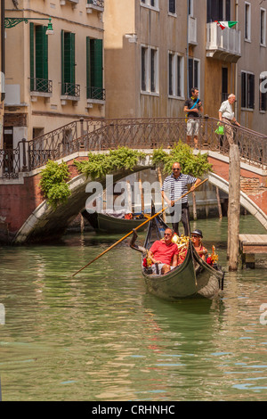 Ein Gondoliere Lenkung seine Gondel mit Passagieren, durch einen kleinen Kanal in Venedig. Stockfoto