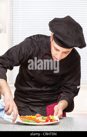 Koch in schwarzer Uniform Rand des einen Obstteller mit Tuch reinigen Stockfoto