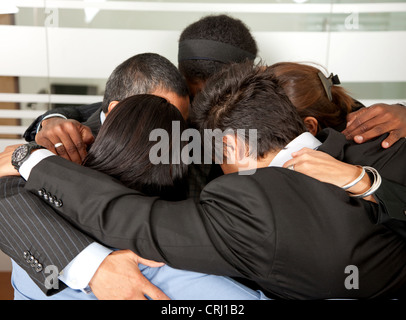 Gruppe von lächelnden jungen Geschäftsleute halten einander an den Schultern stecken ihre Köpfe zusammen Stockfoto