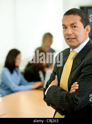 Business-Mann mit verschränkten Armen und Menschen im Hintergrund arbeitet an einem laptop Stockfoto