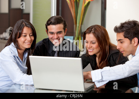 4 lächelnde junge Geschäftsleute um einen laptop Stockfoto