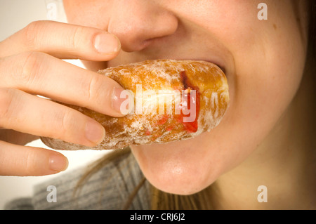 Ein junges Weibchen einen Marmelade Krapfen zu essen. Marmelade-Donuts sind von Junk-Food-Aktivisten im globalen Kampf gegen Fettleibigkeit als fehlerhaft gekennzeichnet mit schlechten Nährwert kritisiert worden. Der Begriff "Junk-e-food'was, geprägt von Michael Jacobson, Direktor des Zentrums für Wissenschaft im öffentlichen Interesse, um Nahrung zu beschreiben, die enthaltenen enthalten hohe Mengen an gesättigten Fetten, Salz oder Zucker ein Stockfoto