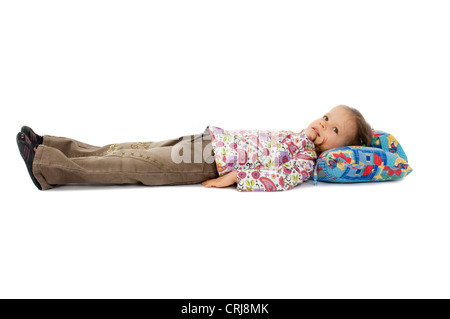 kleines Mädchen liegend auf dem Boden auf dem Rücken, die Arme dicht am Körper und den Kopf auf ein Sitzkissen Stockfoto