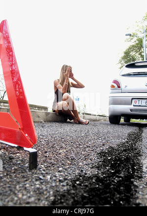 Junge, blonde Frau sitzt am Straßenrand neben ihr Auto telefonieren per Handy während gestikulierend aufgeschlüsselt Stockfoto