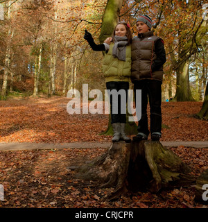 Ein Mädchen und ein Junge auf einem Baumstamm stehend und deutete auf etwas in einem Park im Herbst Stockfoto