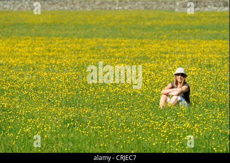 Eine Mädchen sitzt auf einer Wiese Gebiet der gelben Butterblume Blumen an Bampton, Cumbria Stockfoto