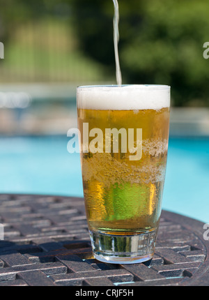 Schlichte Pint Glas Bier, sitzen am Tisch von blauen Swimmingpool gegossen Stockfoto