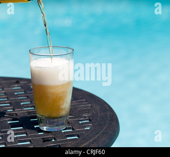 Schlichte Pint Glas Bier, sitzen am Tisch von blauen Swimmingpool gegossen Stockfoto