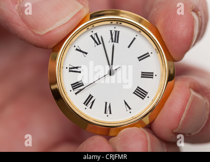 Kleine gold farbigen Uhr fast um Mitternacht von Fingerspitzen gehalten Stockfoto