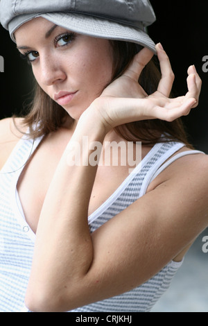 Brünette junge Frau posiert kokett mit der Hand an der Spitze der Mütze auf der Seite Stockfoto