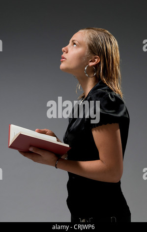 stilvolle blondes junges Mädchen mit einem Buch in Händen nach oben stehend in Gedanken versunken Stockfoto