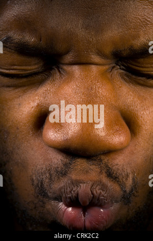 Ein junger Mann drückt seine Augen geschlossen, als auch drückte seine Lippen fest geschlossen. Stockfoto