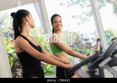 Junge Frauen reden und lachen während der Arbeit am Heimtrainer im Wellnessclub Stockfoto