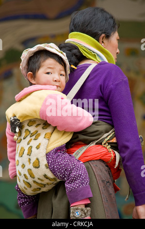 Eine tibetische chinesische Mutter mit ihrem Baby auf dem Rücken im Kloster Labrang in Xiahe. Stockfoto