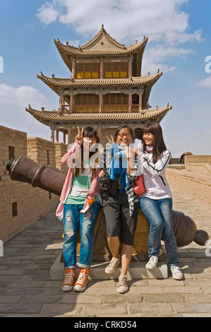 3 chinesische Touristen sitzen auf einem Canon auf der westlichen Seite von Jiayuguan und Jiayuguan Pass Turm im Hintergrund. Stockfoto