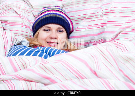 Junge glücklich lächelnde Frau in Wintermütze in Bettdecke gewickelt. Stockfoto